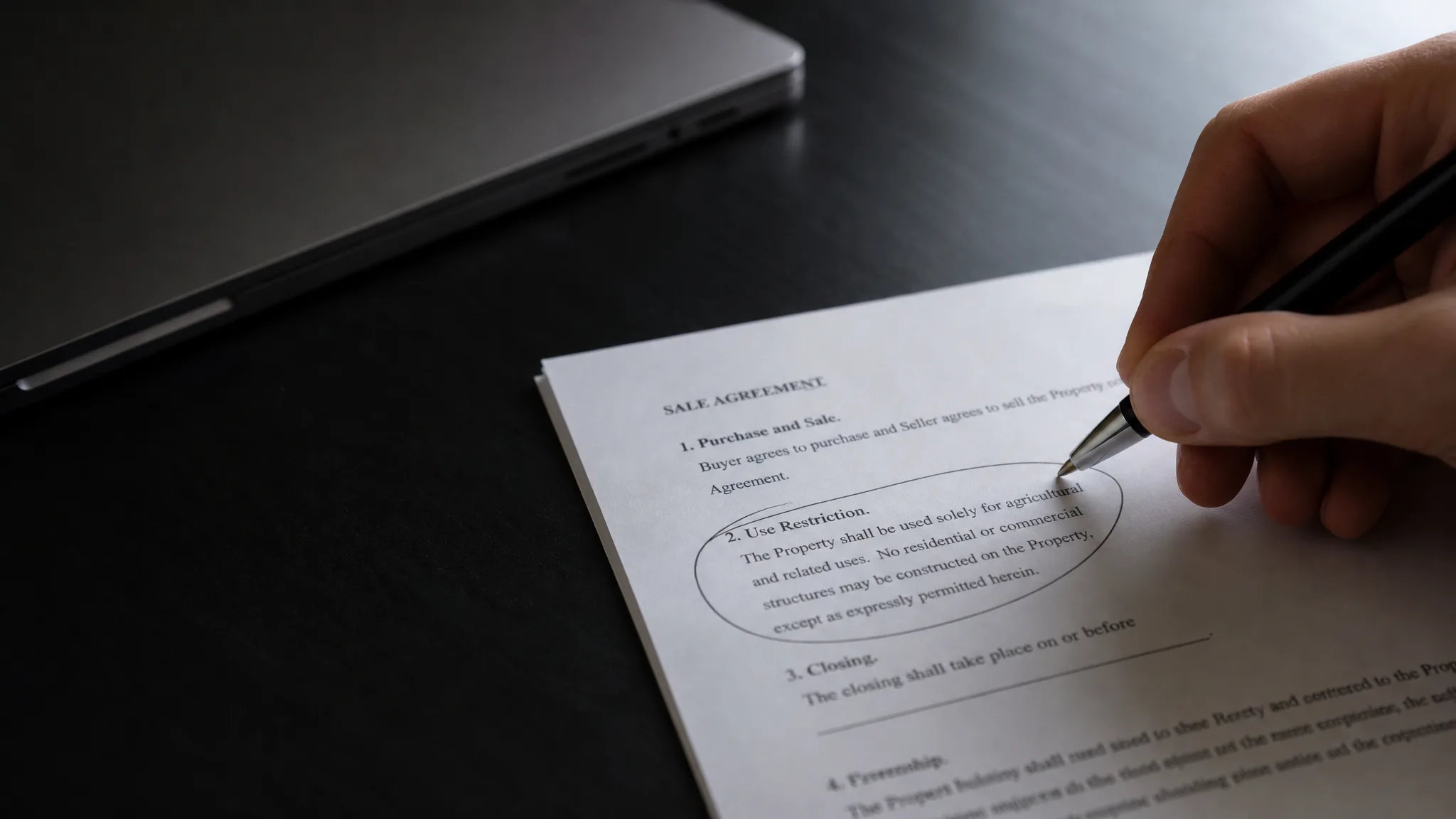 Hand marking a narrow section of a sale agreement to symbolize non-compete terms in a SaaS acquisition
